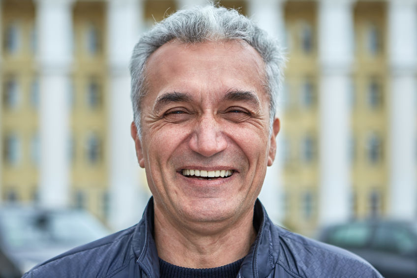 Closeup laughing face of an elderly businessman, civil servant, doctor or television presenter. Portrait of a joyful caucasian man over fifty years, with short gray hair outdoors, near public building